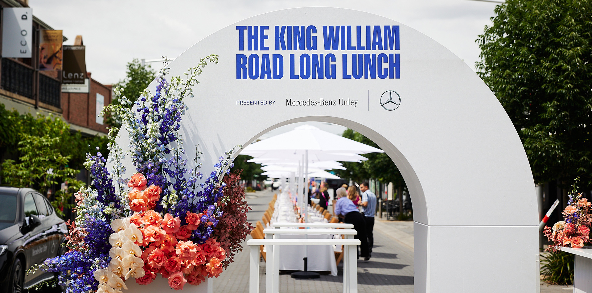 A vibrant outdoor dining scene on King William Road, featuring tables set for a long lunch with guests enjoying their meals.